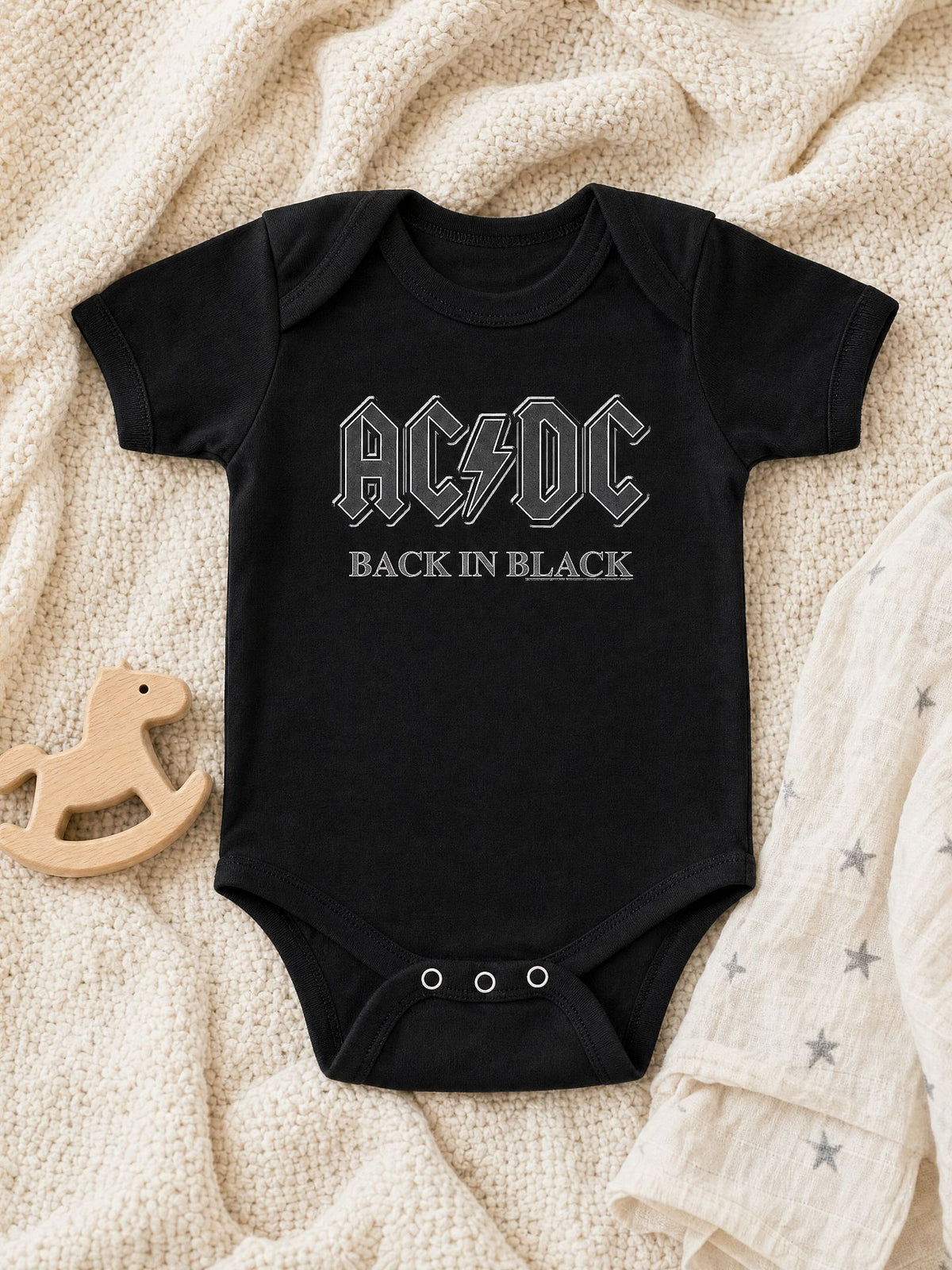 AC/DC Back In Black infant bodysuit laid flat on a cream knit blanket. AI-generated flat-lay image.