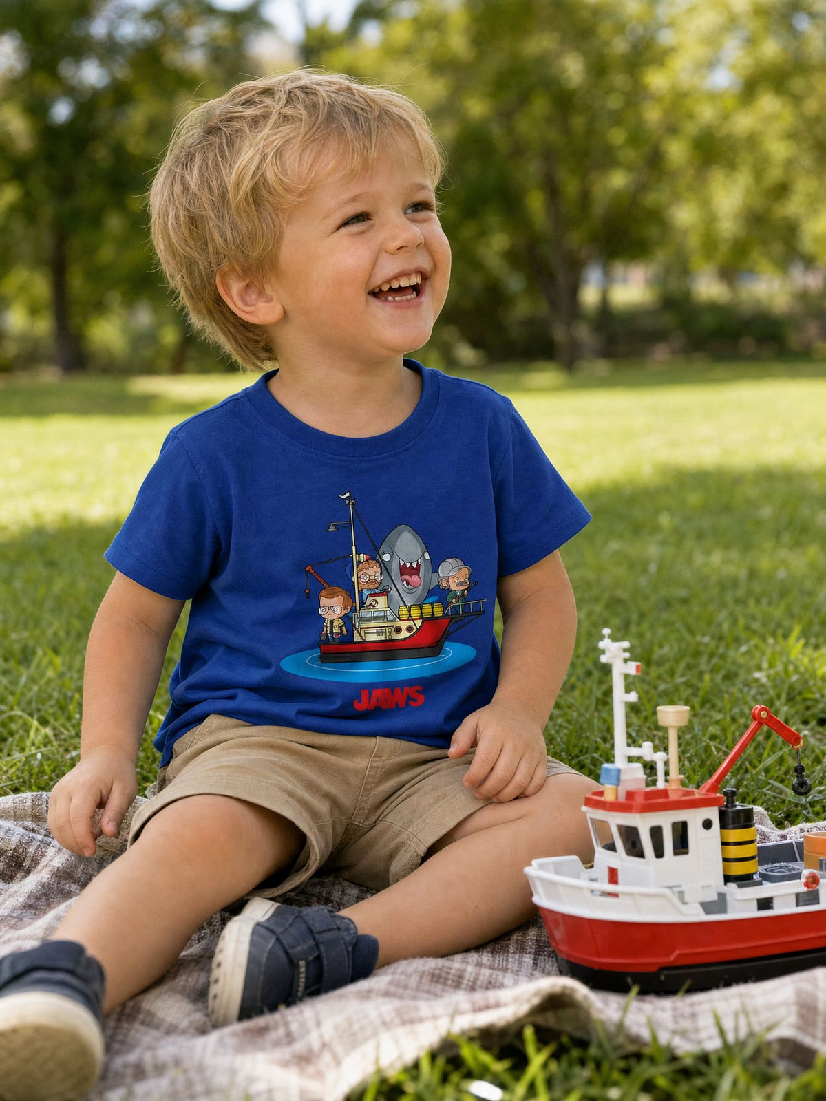 Toddler wearing the officially licensed Jaws kawaii boat toddler T-shirt on a picnic blanket. AI-generated lifestyle image.